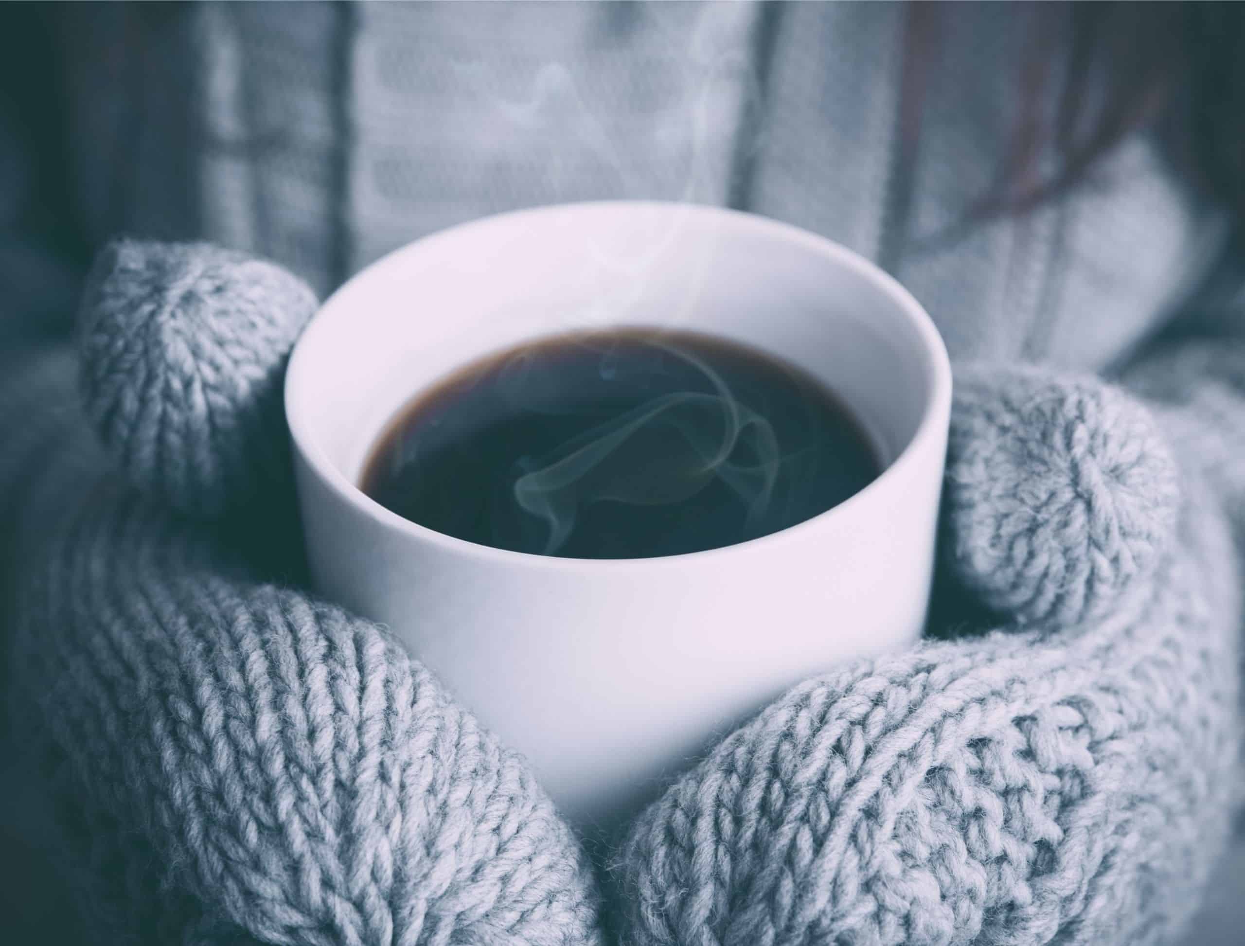 Cold mitten hands holding cup of coffee